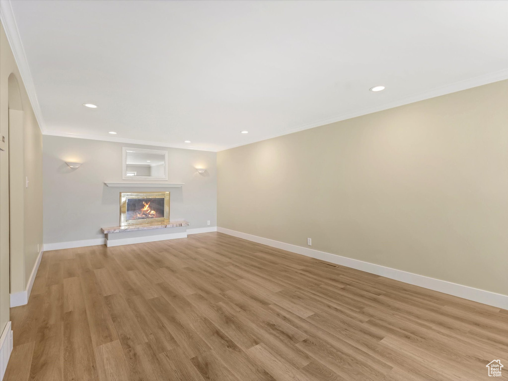 Unfurnished living room featuring crown molding, light wood finished floors, recessed lighting, baseboards, and a glass covered fireplace