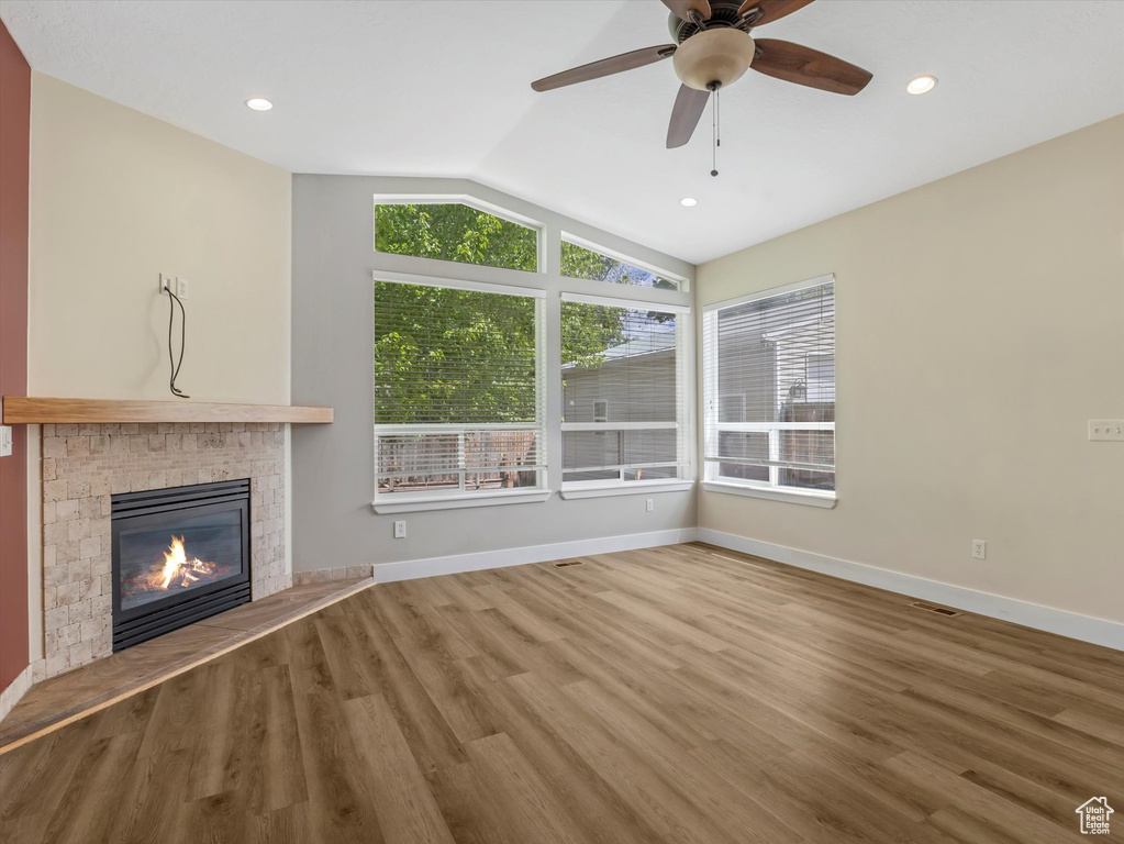 Unfurnished living room with vaulted ceiling, plenty of natural light, wood finished floors, a glass covered fireplace, and recessed lighting