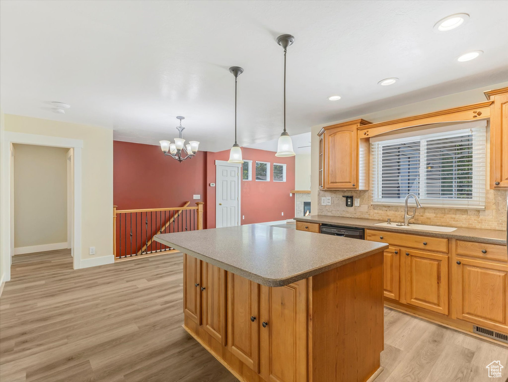 Kitchen with a sink, light wood-style floors, a center island, decorative backsplash, and pendant lighting