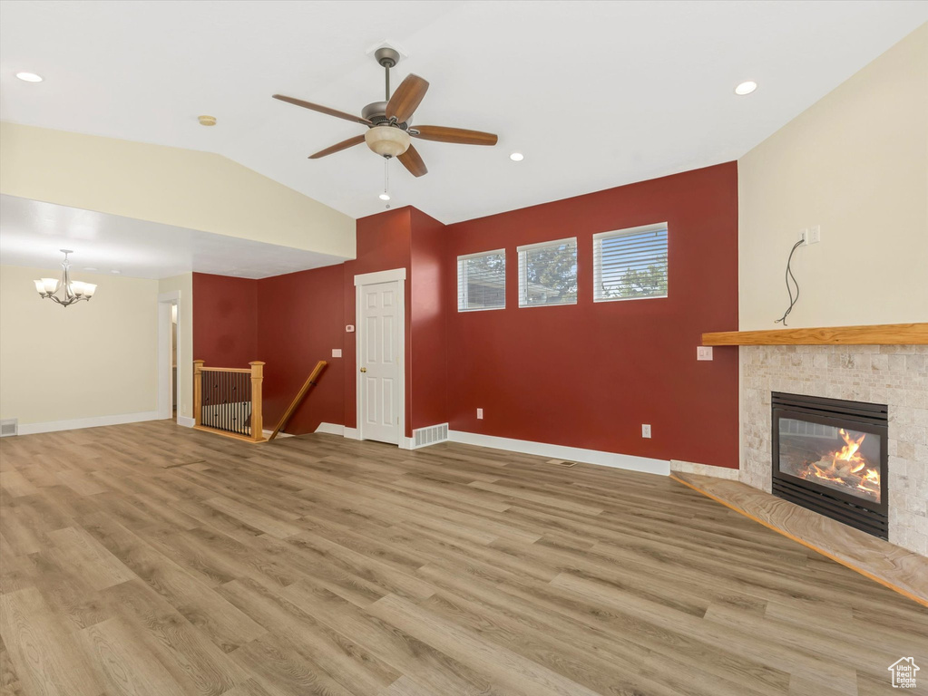Unfurnished living room featuring a chandelier, wood finished floors, a tiled fireplace, vaulted ceiling, and ceiling fan