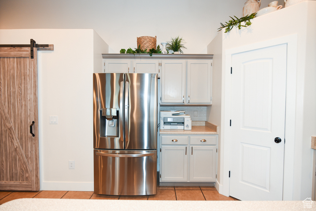 Kitchen with stainless steel fridge, light tile patterned floors, light countertops, a barn door, and tasteful backsplash