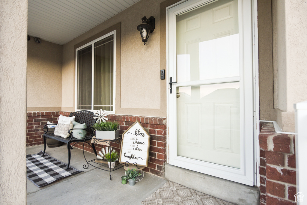 Property entrance featuring covered porch, brick siding, and stucco siding
