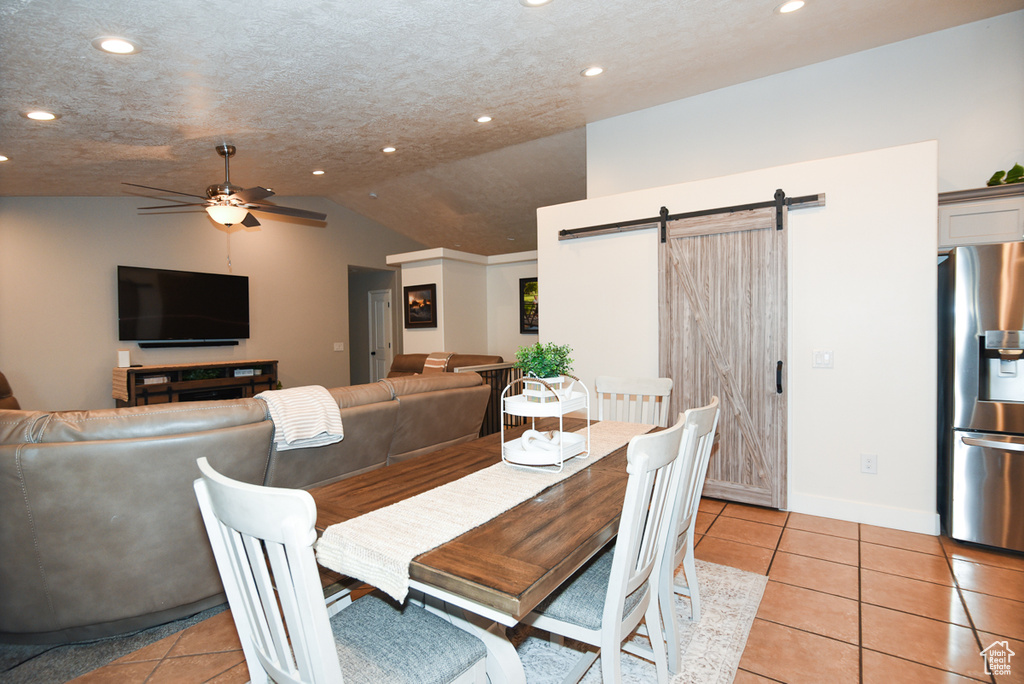 Dining area featuring a barn door, ceiling fan, recessed lighting, light tile patterned flooring, and vaulted ceiling