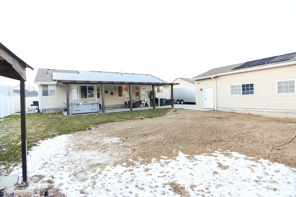 Snow covered back of property with roof mounted solar panels and a patio