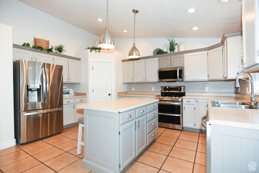 Kitchen featuring stainless steel appliances, a sink, a kitchen island, decorative backsplash, and light countertops