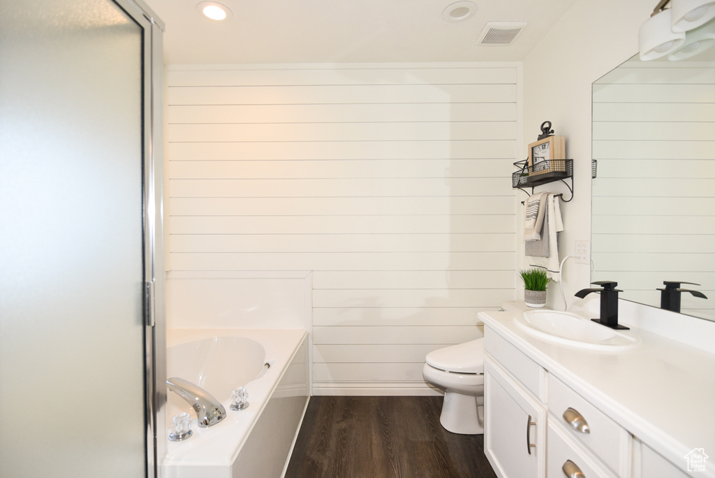 Bathroom with a garden tub, wood finished floors, vanity, toilet, and recessed lighting
