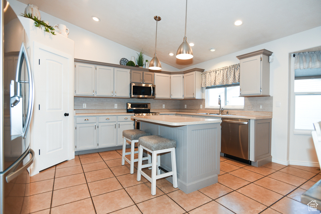 Kitchen featuring appliances with stainless steel finishes, a sink, decorative backsplash, a kitchen island, and light tile patterned floors