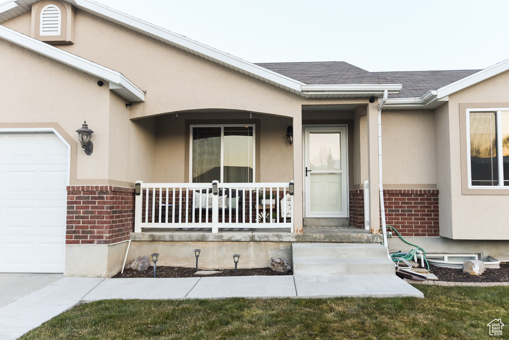 Entrance to property featuring brick siding, a porch, stucco siding, a garage, and roof with shingles