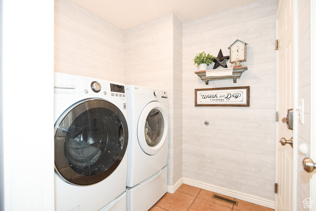 Laundry area with washer and clothes dryer, light tile patterned floors, and wood walls