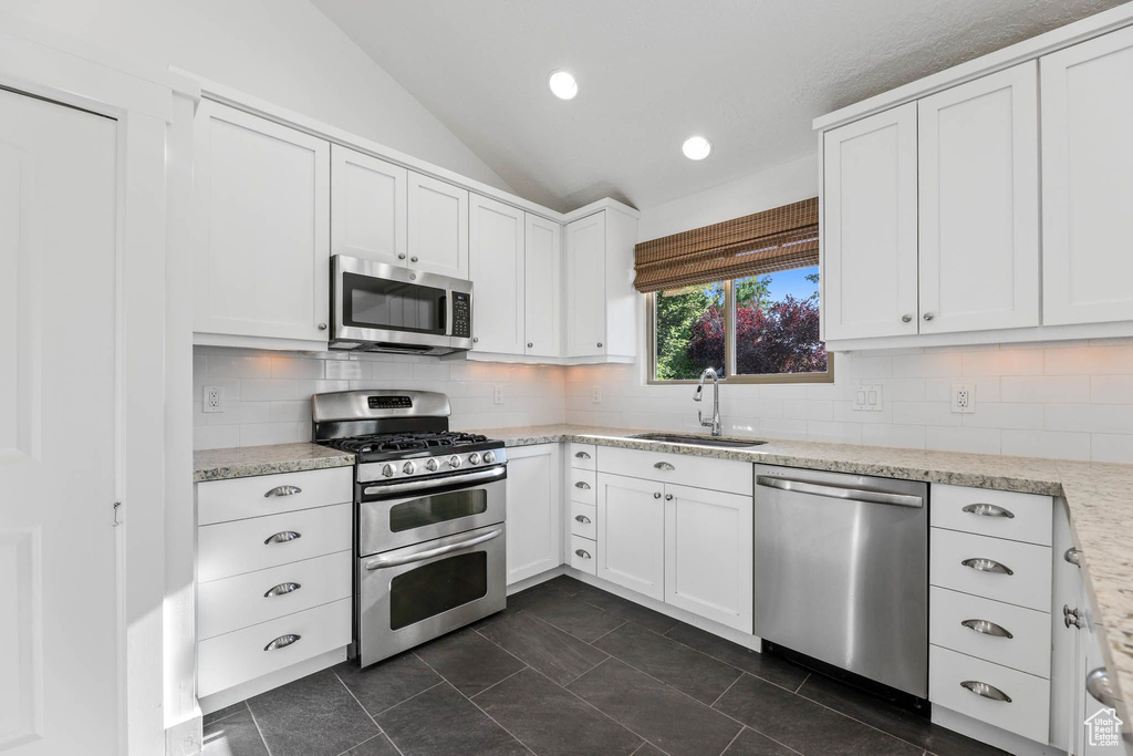 Kitchen with stainless steel appliances, a sink, vaulted ceiling, white cabinetry, and decorative backsplash