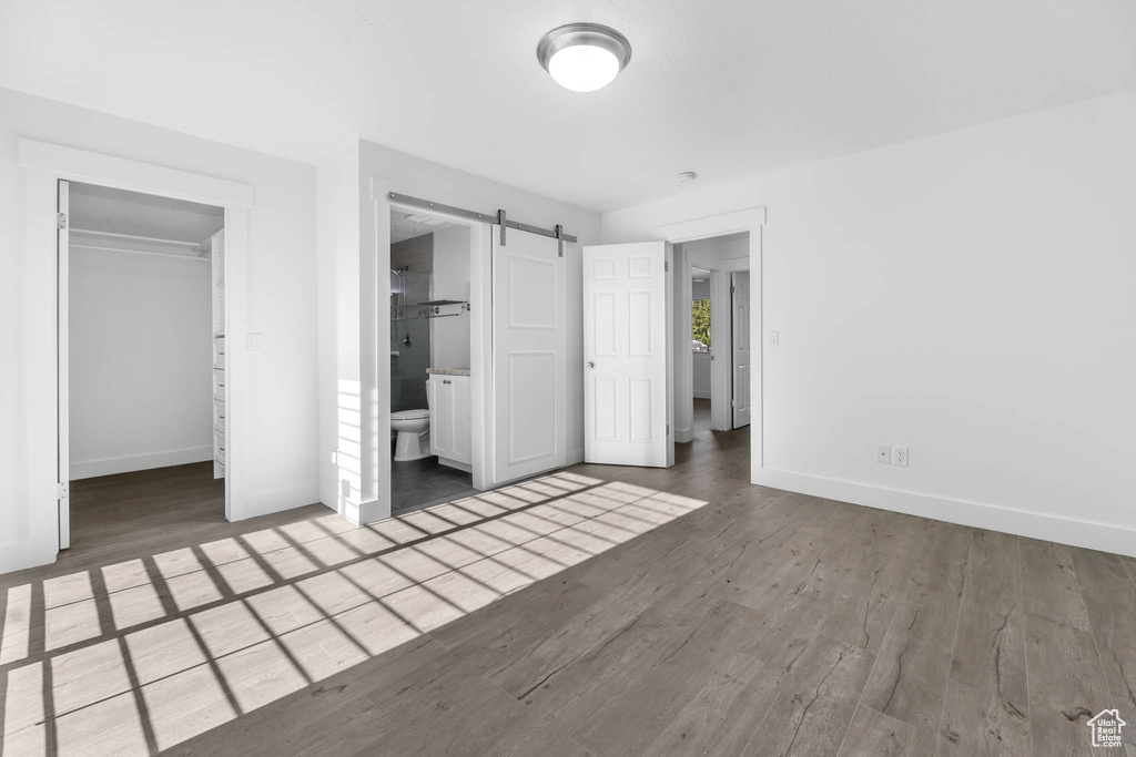 Unfurnished bedroom featuring baseboards, wood finished floors, a walk in closet, a barn door, and a closet