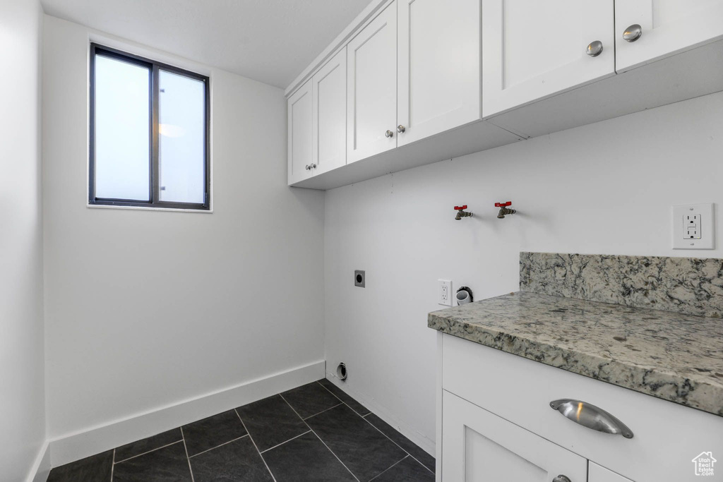 Laundry room with electric dryer hookup, cabinet space, baseboards, and dark tile patterned floors