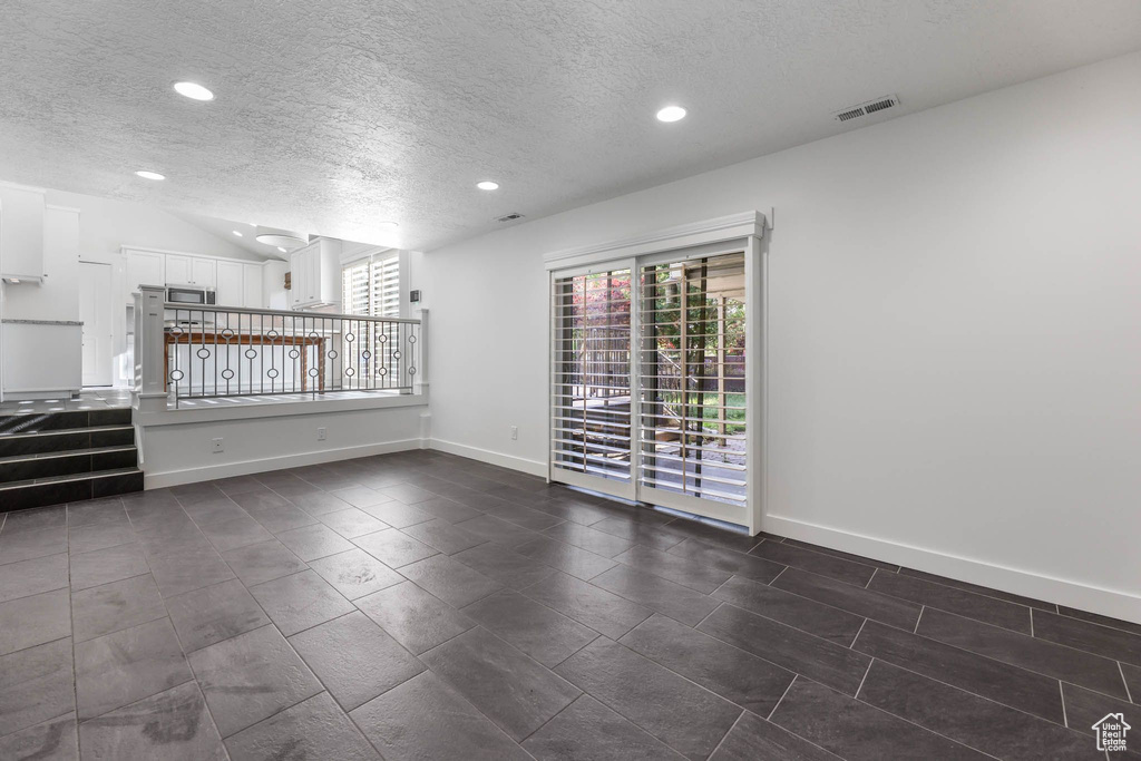 Spare room featuring a textured ceiling, plenty of natural light, recessed lighting, baseboards, and dark tile patterned floors