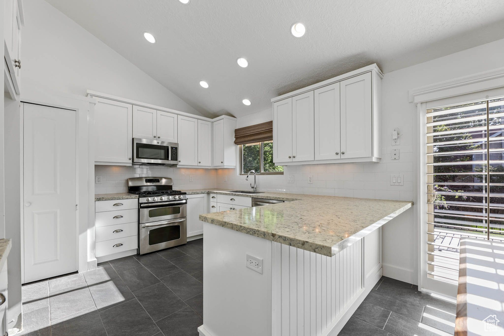 Kitchen featuring appliances with stainless steel finishes, a sink, a peninsula, lofted ceiling, and white cabinets