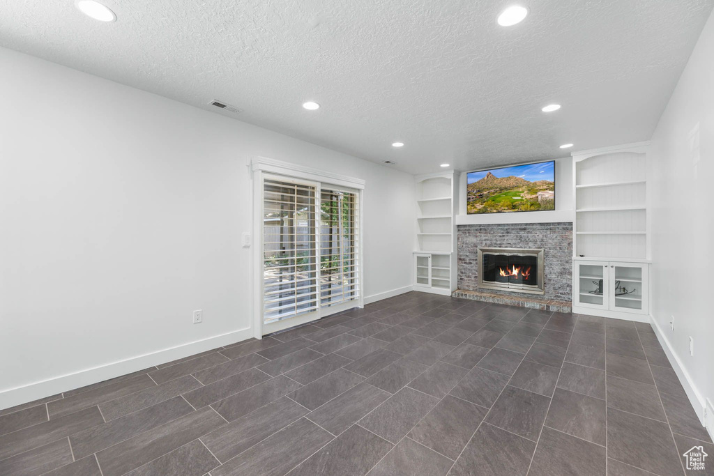 Unfurnished living room with a textured ceiling, baseboards, recessed lighting, a glass covered fireplace, and built in shelves