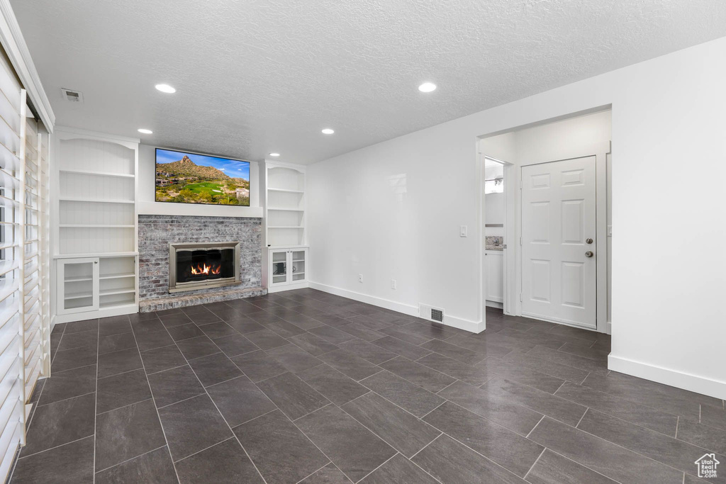 Unfurnished living room featuring a fireplace, a textured ceiling, built in shelves, baseboards, and recessed lighting