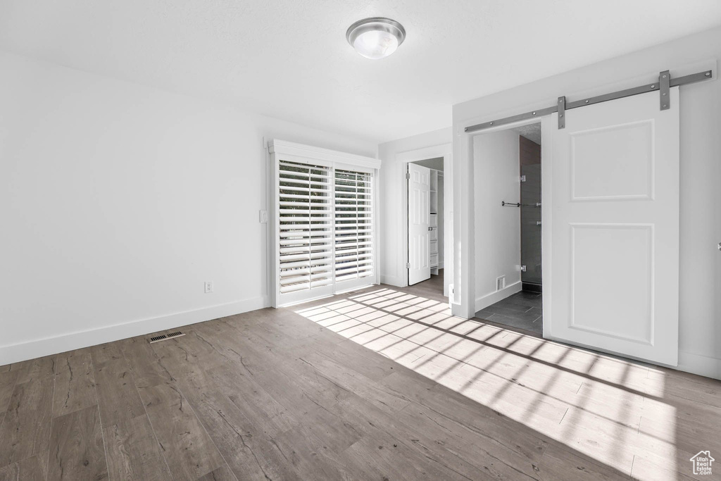 Unfurnished bedroom featuring wood finished floors, a barn door, and baseboards