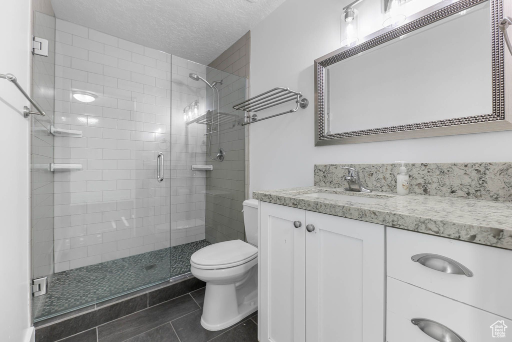 Full bathroom featuring toilet, a stall shower, a textured ceiling, vanity, and tile patterned flooring