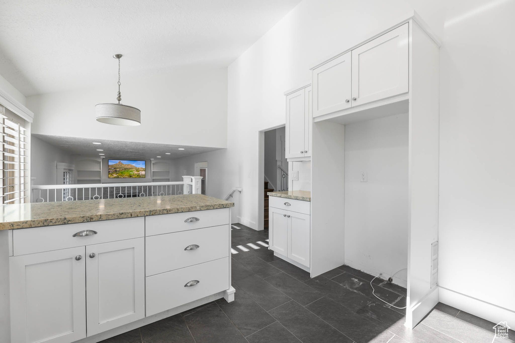 Kitchen with white cabinetry, a towering ceiling, light stone counters, and hanging light fixtures