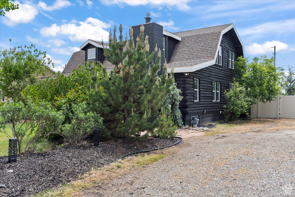 View of property exterior featuring a gambrel roof, a shingled roof, a chimney, and log siding