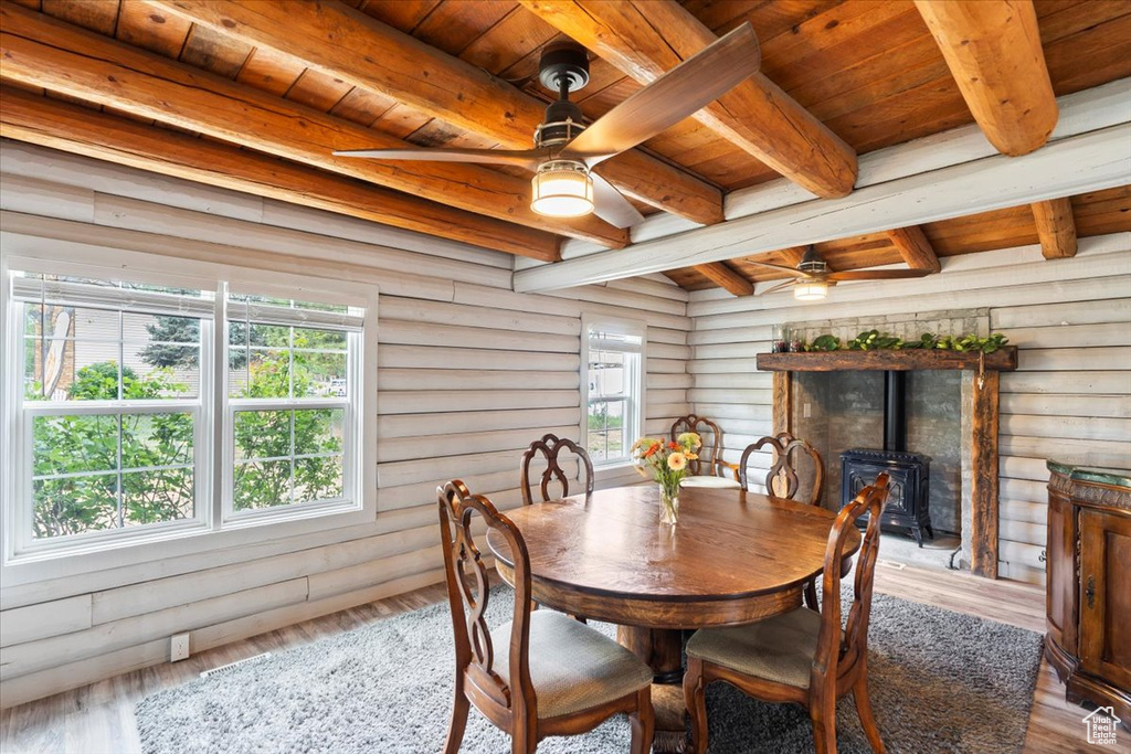 Dining space featuring a wood stove, log walls, a ceiling fan, wood ceiling with exposed beams, and wood finished floors
