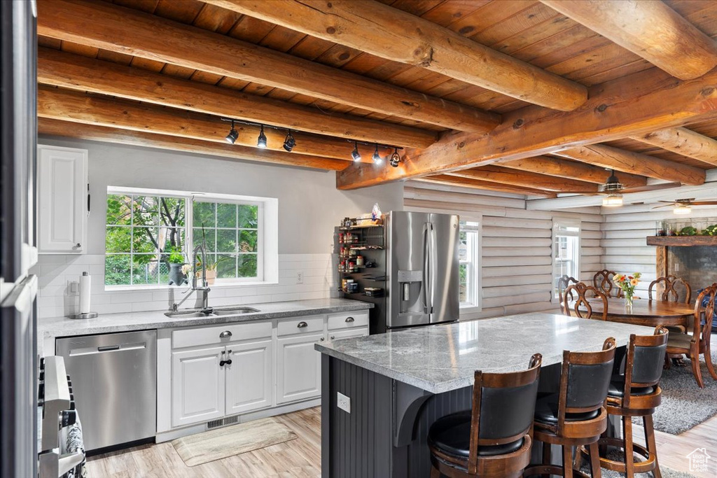 Kitchen with a sink, stainless steel appliances, wooden ceiling with exposed beams, a kitchen breakfast bar, and light stone countertops