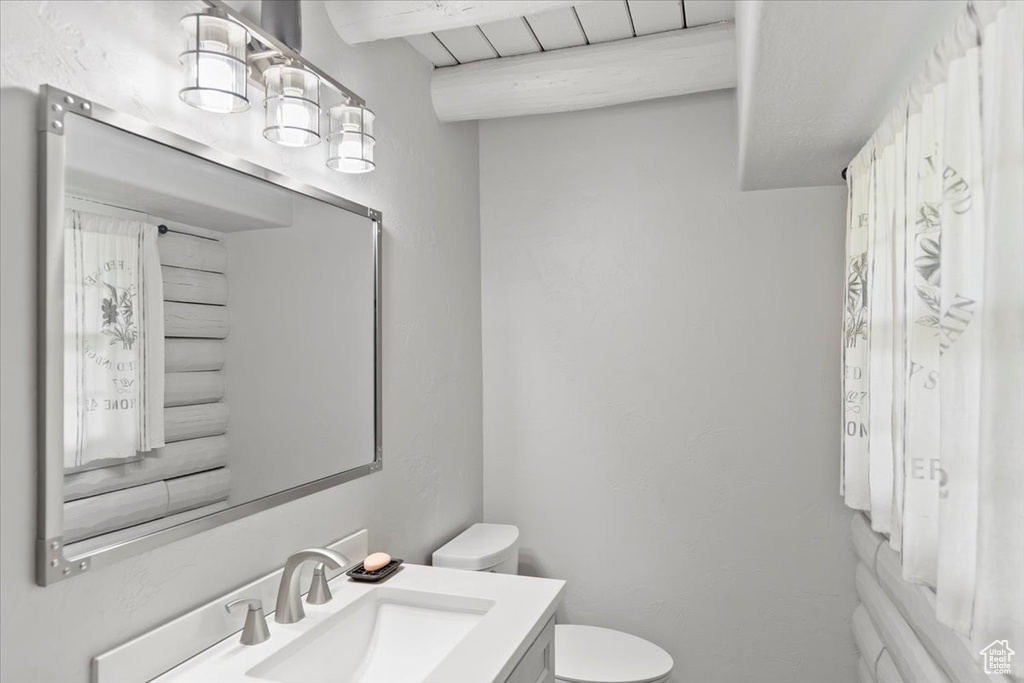Bathroom featuring toilet, vanity, and beamed ceiling