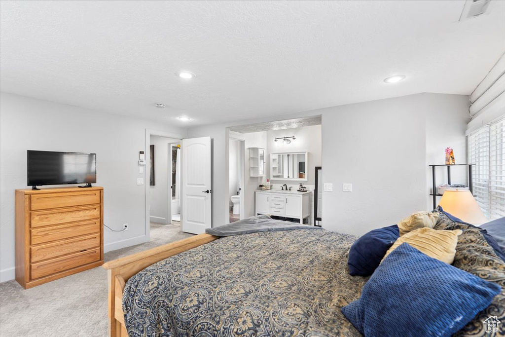 Bedroom with light colored carpet, ensuite bath, baseboards, recessed lighting, and a sink