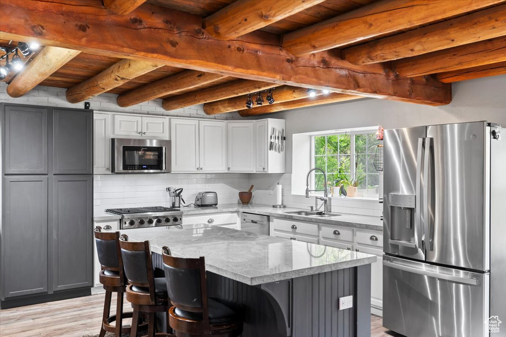 Kitchen with stainless steel appliances, a sink, light stone countertops, backsplash, and light wood-type flooring