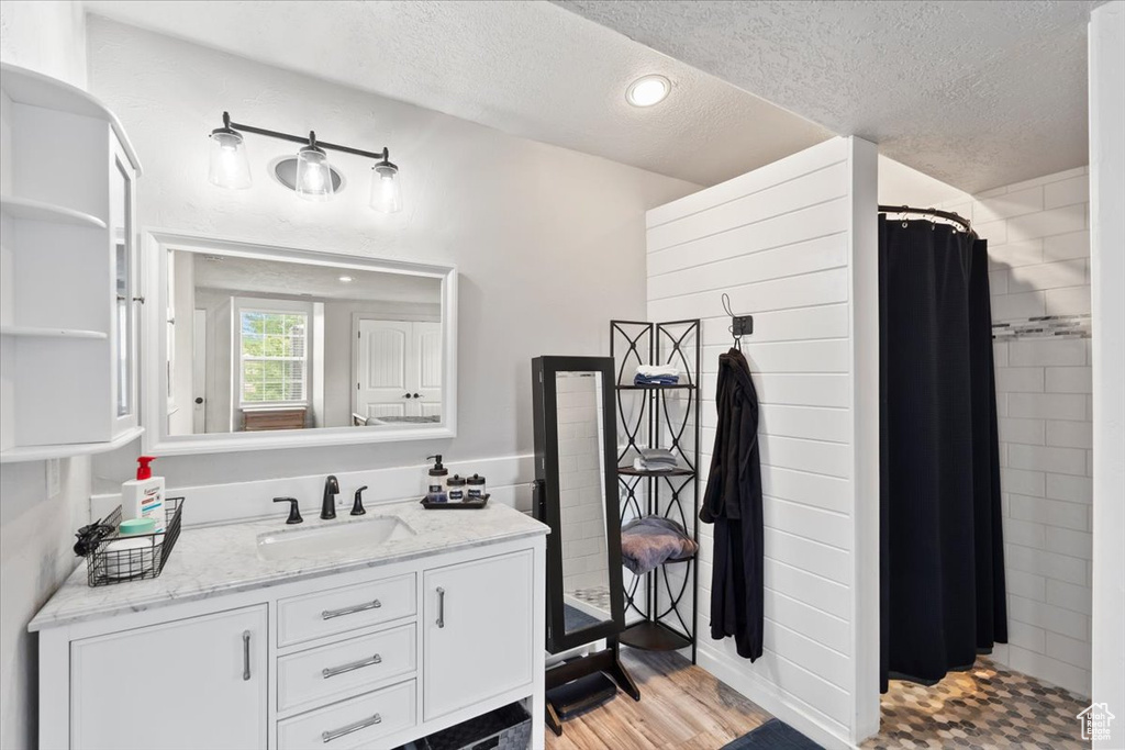 Bathroom featuring a textured ceiling, a shower with shower curtain, vanity, wood finished floors, and recessed lighting