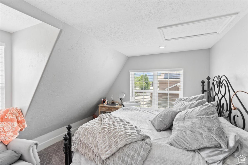 Carpeted bedroom with attic access, a textured ceiling, and lofted ceiling