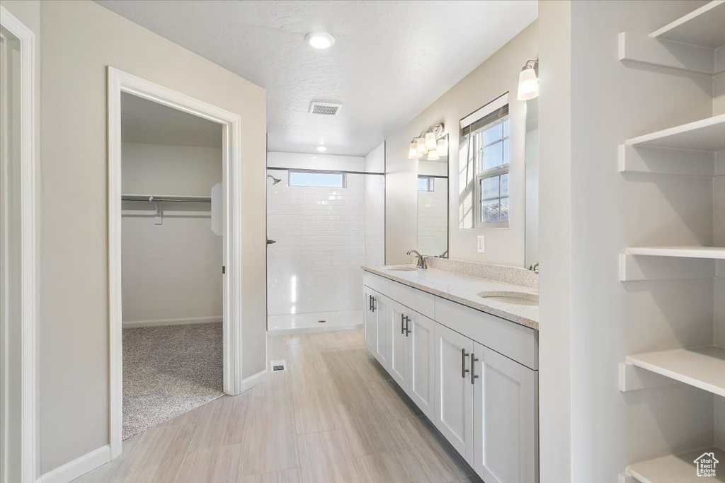Full bathroom with a stall shower, a walk in closet, double vanity, and baseboards