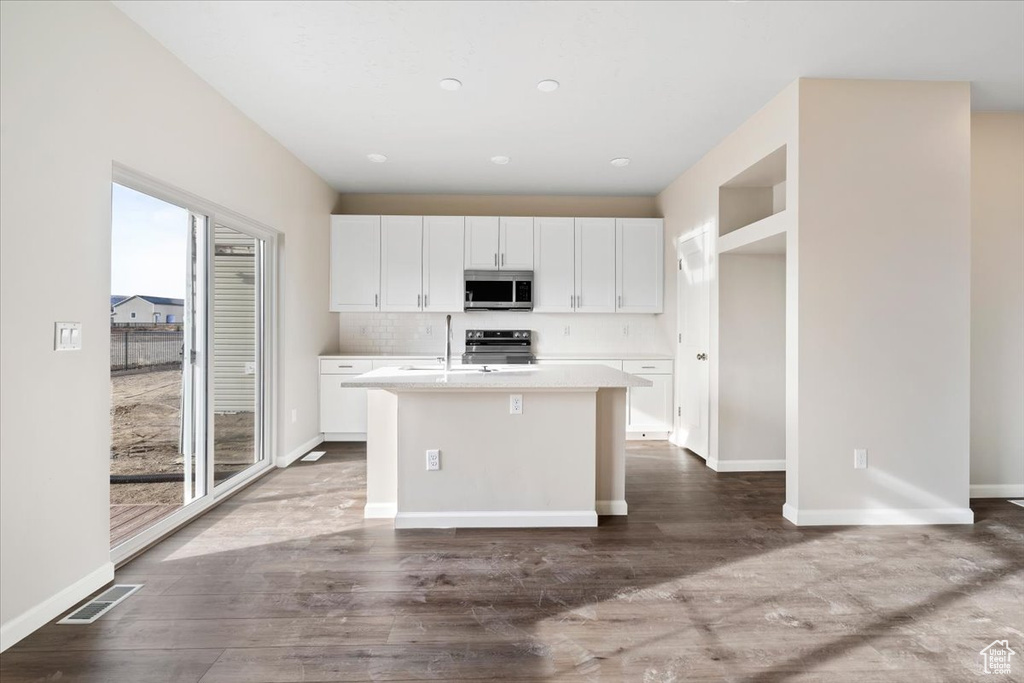 Kitchen with appliances with stainless steel finishes, white cabinets, an island with sink, and light countertops