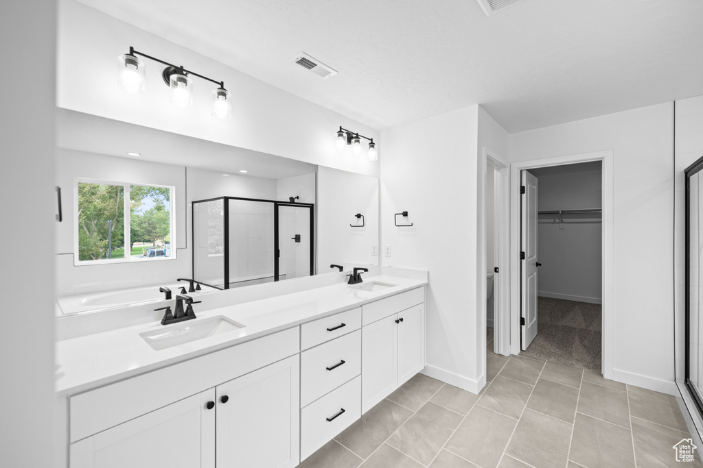 Full bathroom featuring a stall shower, double vanity, a walk in closet, tile patterned floors, and baseboards