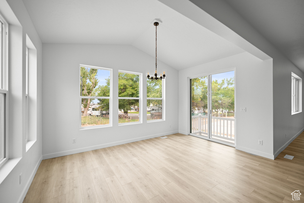 Unfurnished dining area with a chandelier, light wood finished floors, baseboards, and lofted ceiling