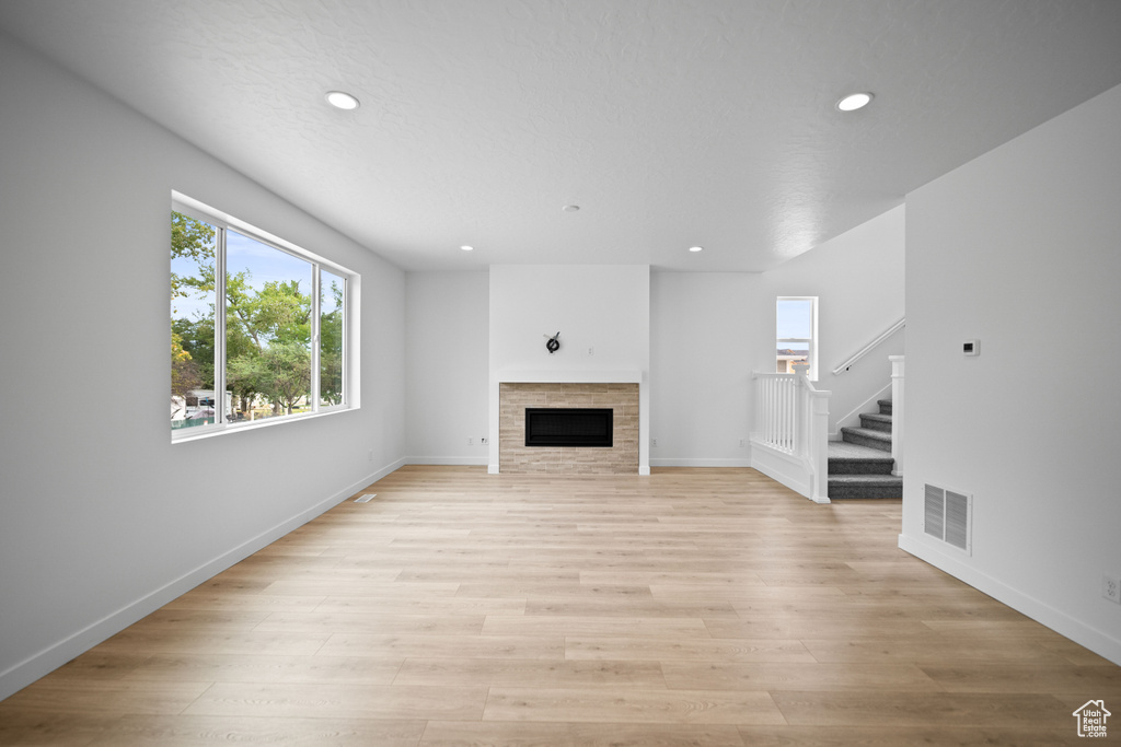 Unfurnished living room with stairway, recessed lighting, a tile fireplace, light wood-style flooring, and baseboards