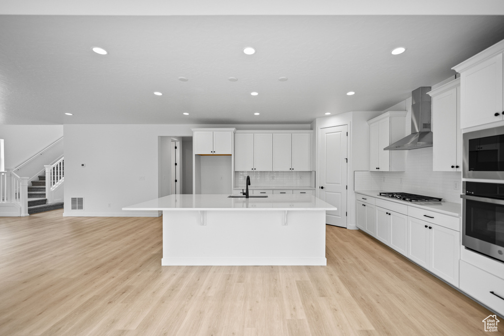 Kitchen with wall chimney range hood, stainless steel appliances, a sink, recessed lighting, and a kitchen island with sink