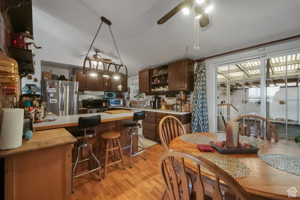 Dining area featuring ceiling fan, light wood finished floors, and vaulted ceiling