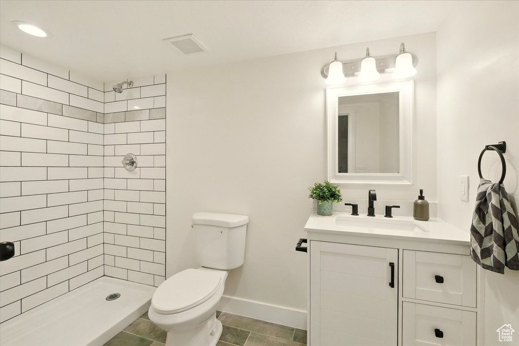 Bathroom with toilet, vanity, a tile shower, and baseboards