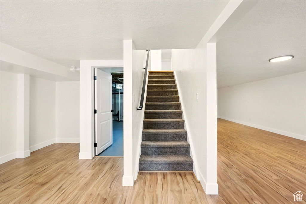Staircase with wood finished floors, baseboards, and a textured ceiling