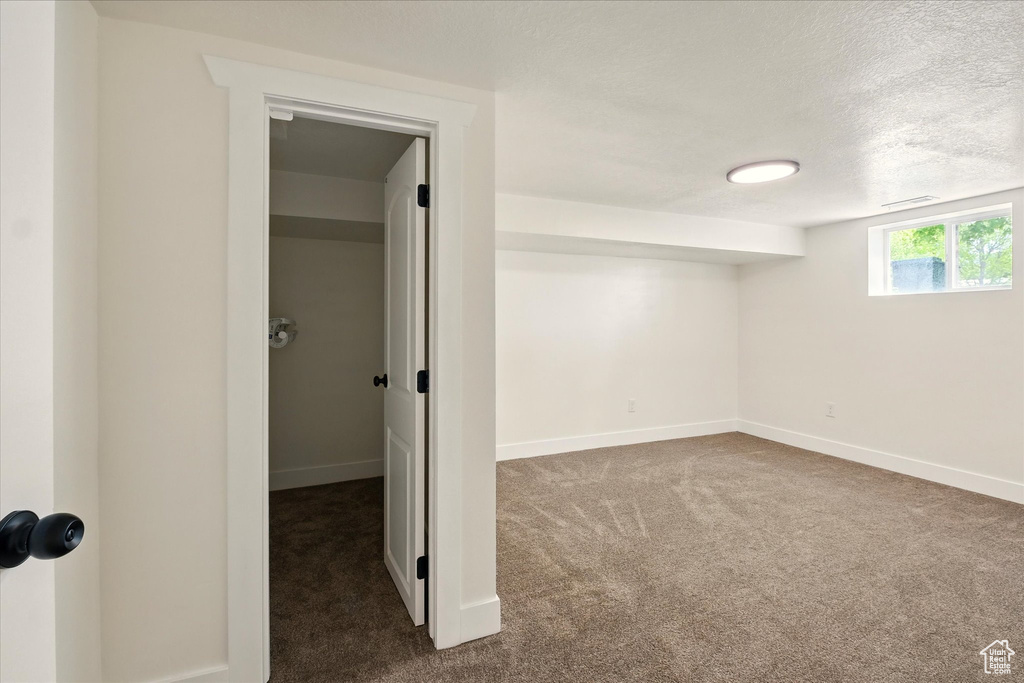 Below grade area featuring dark colored carpet, baseboards, and a textured ceiling