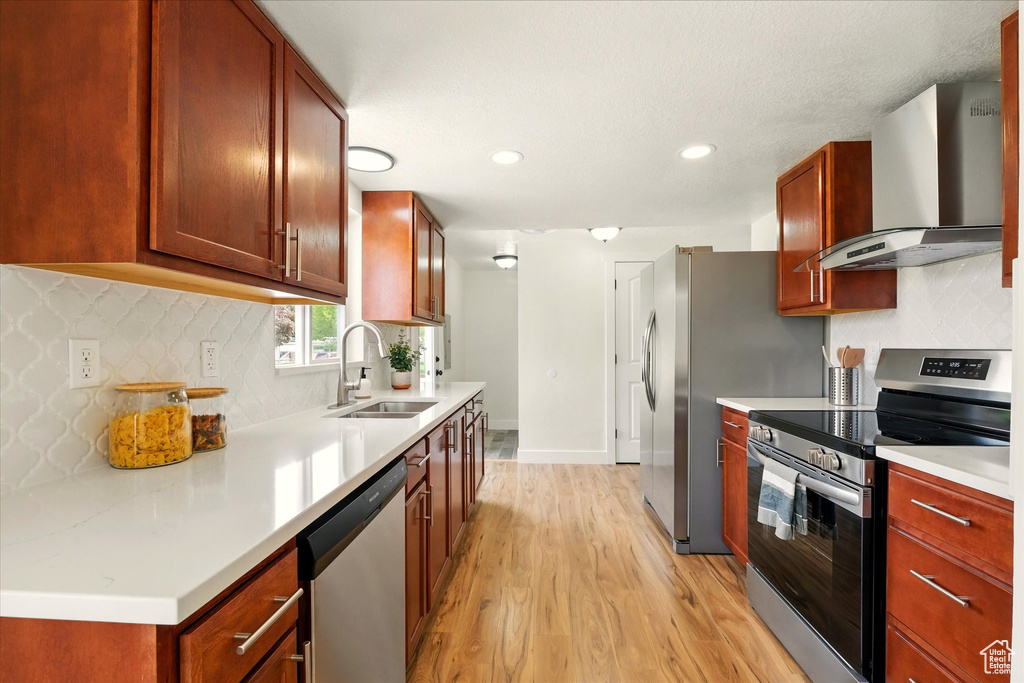 Kitchen featuring stainless steel appliances, wall chimney range hood, a sink, light wood-style flooring, and tasteful backsplash