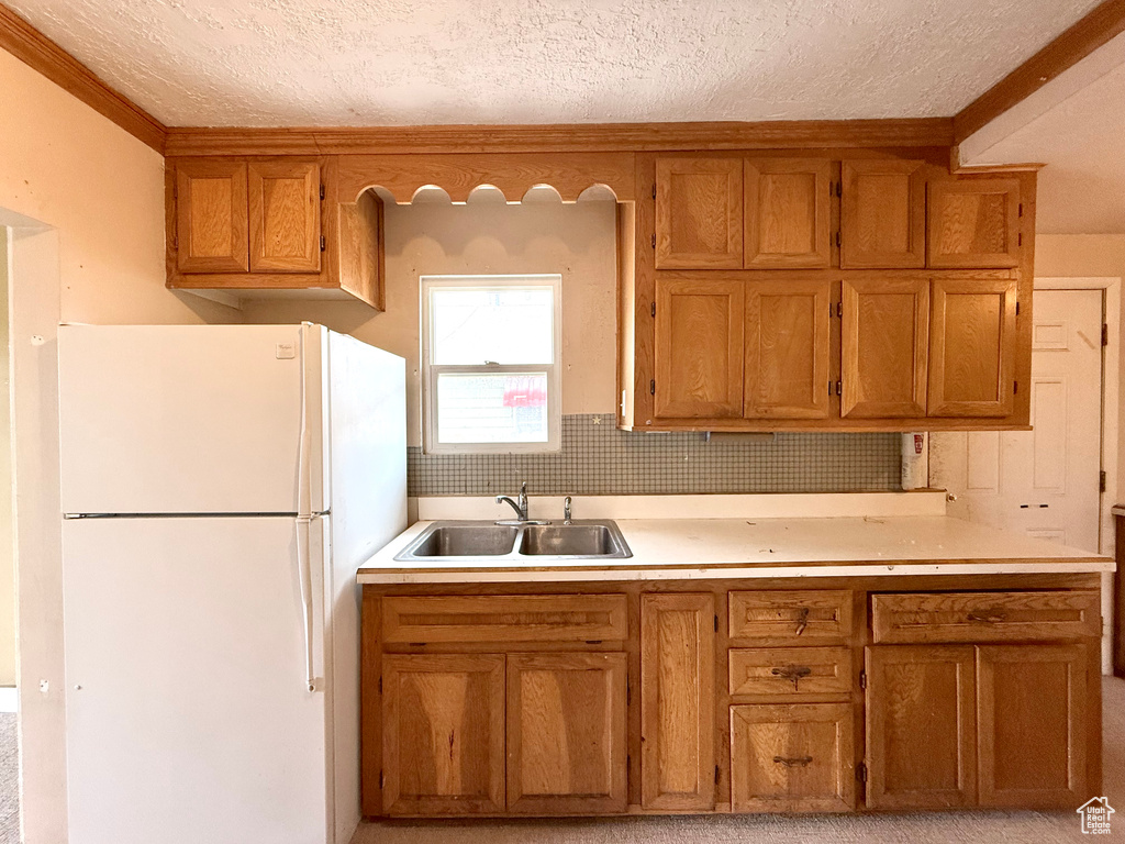 Kitchen with freestanding refrigerator, a sink, a textured ceiling, brown cabinetry, and light countertops