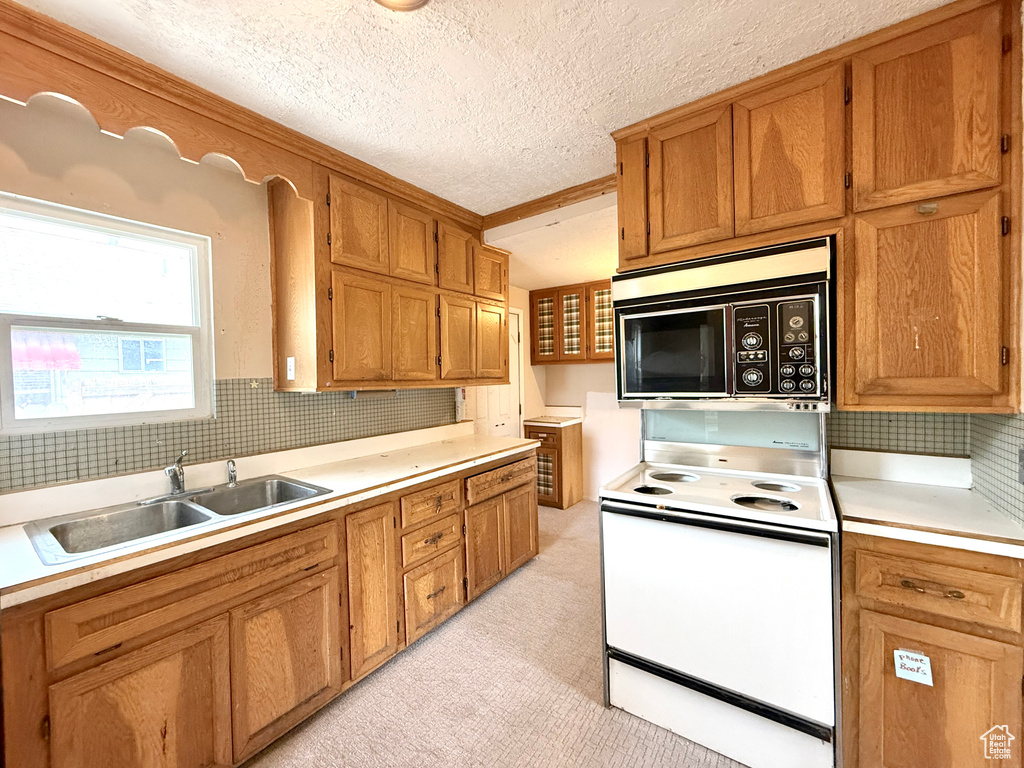 Kitchen with electric stove, a sink, light countertops, backsplash, and brown cabinets
