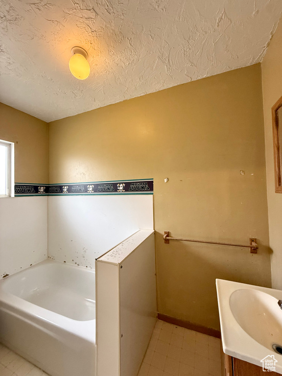 Full bathroom with a bath, a textured ceiling, vanity, and baseboards