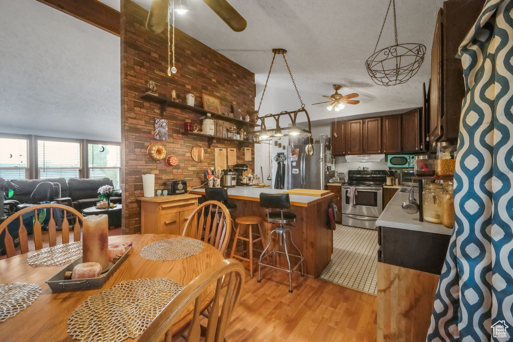 Dining area featuring a ceiling fan, brick wall, light wood-style flooring, a textured ceiling, and vaulted ceiling