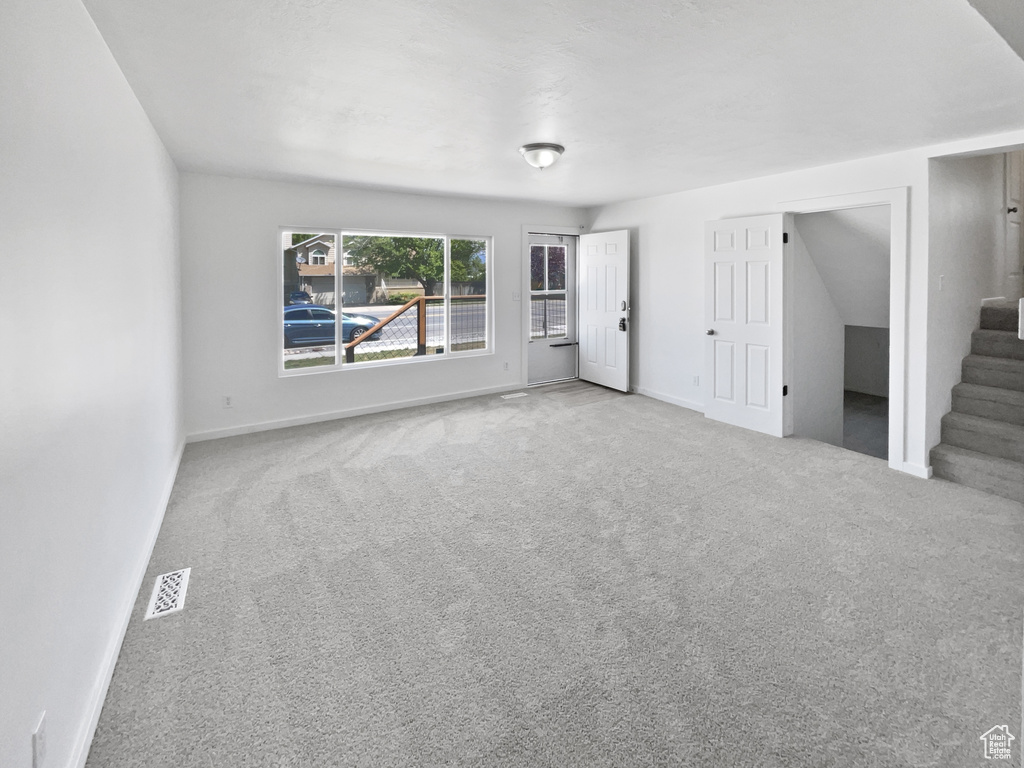 Unfurnished living room featuring carpet floors, baseboards, and stairs