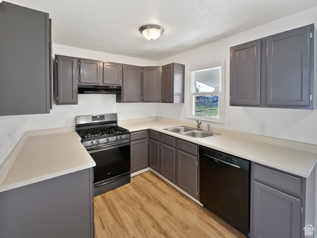 Kitchen featuring stainless steel gas range oven, a sink, black dishwasher, under cabinet range hood, and light wood finished floors