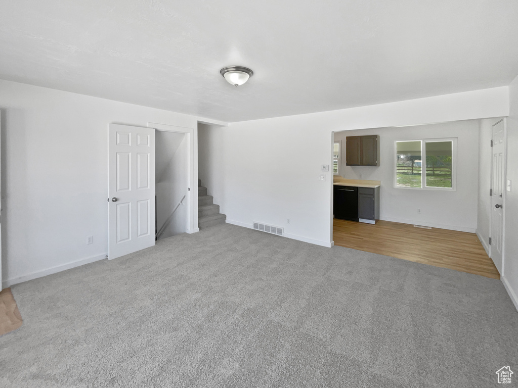 Unfurnished living room featuring light carpet, stairway, and baseboards