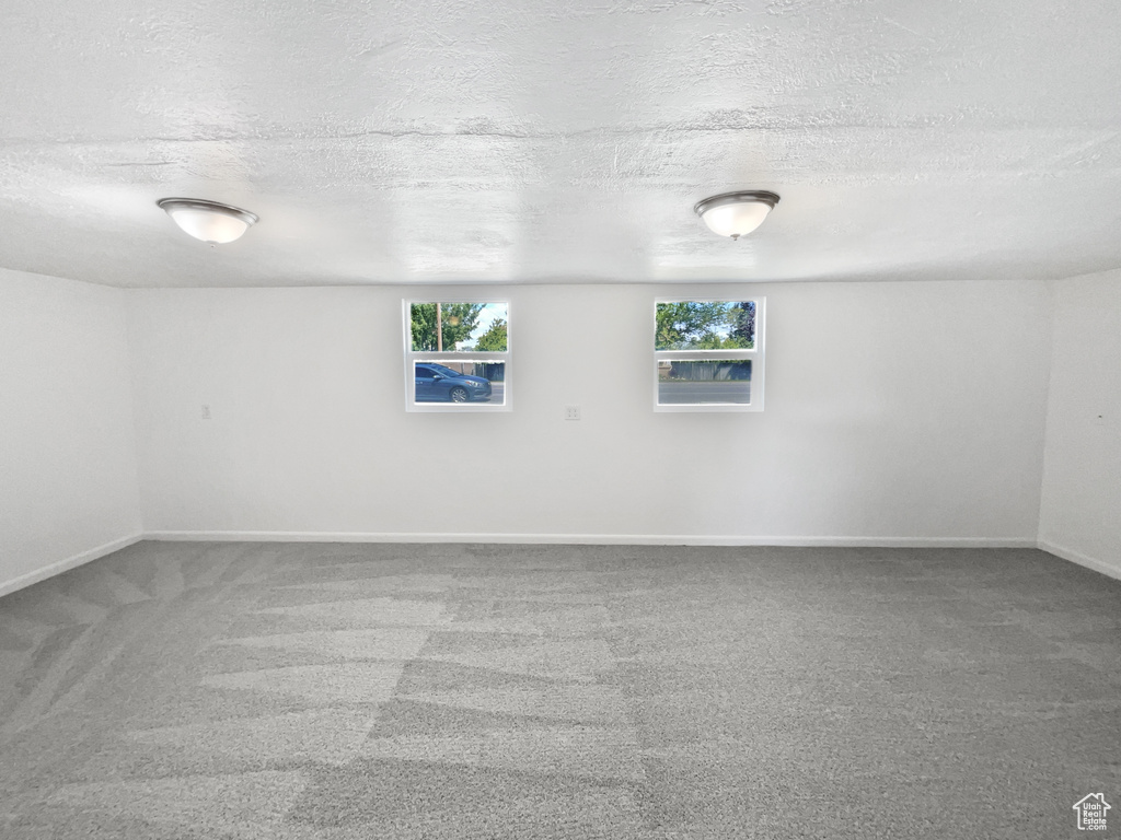 Carpeted empty room featuring a textured ceiling and baseboards